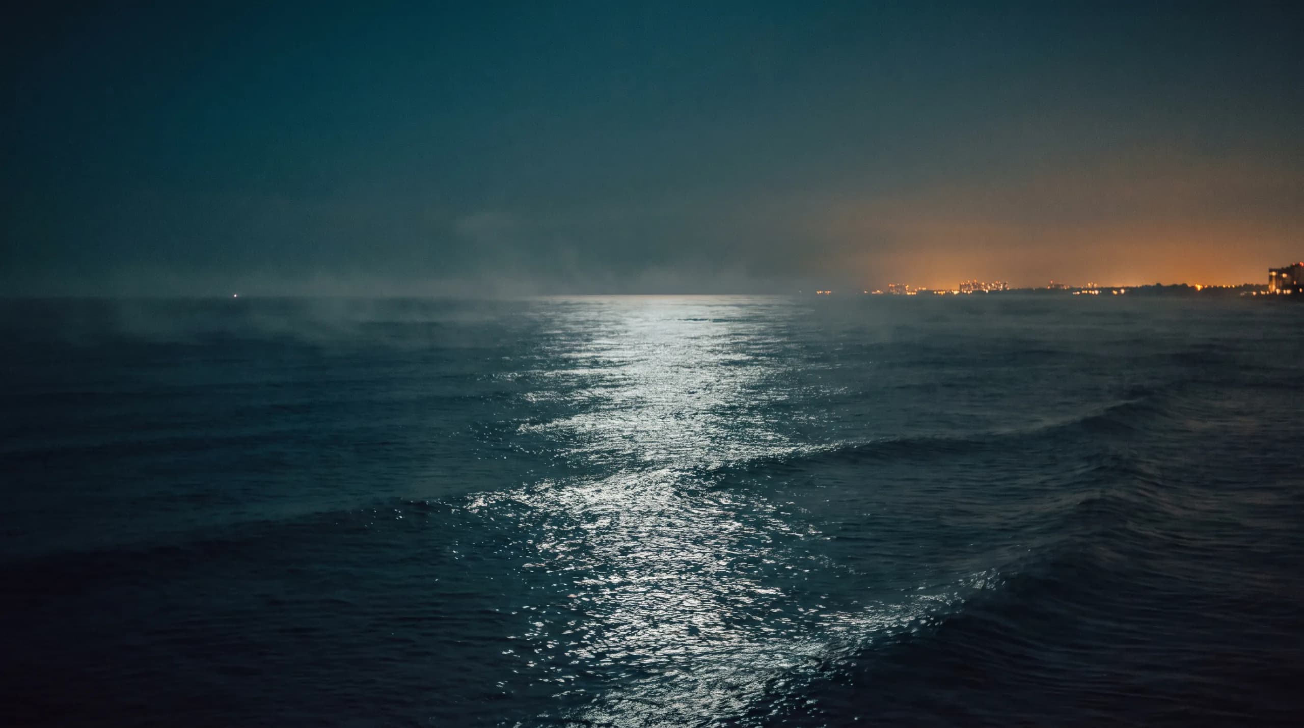 Moonlit dark ocean at dusk off the South Florida coast, city lights on the horizon