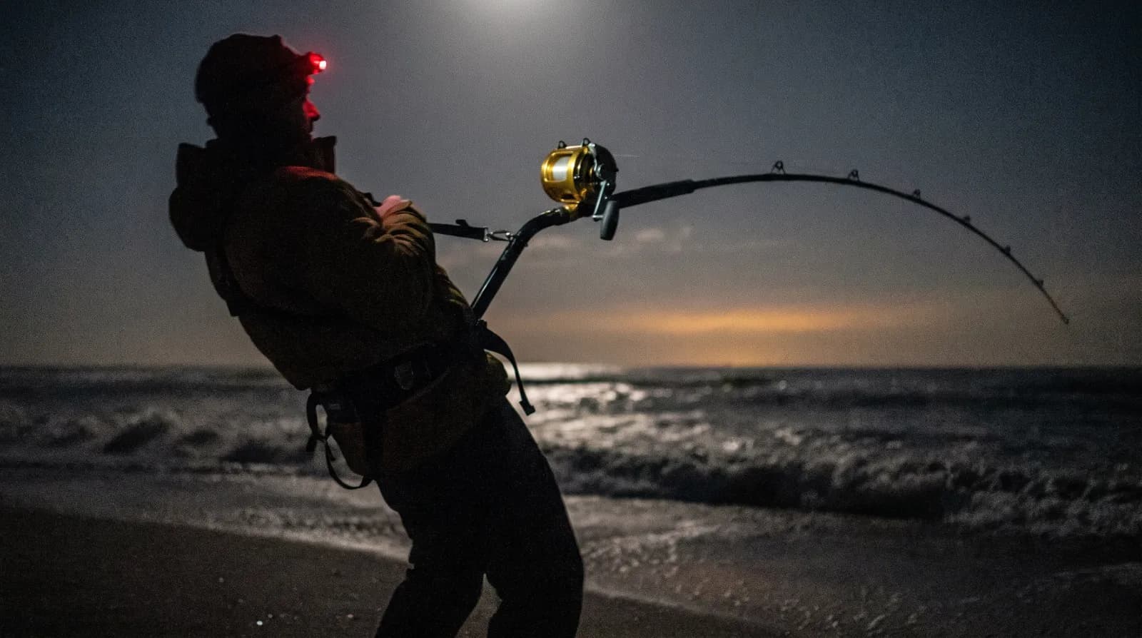 Angler clipped into a fighting harness on a dark beach